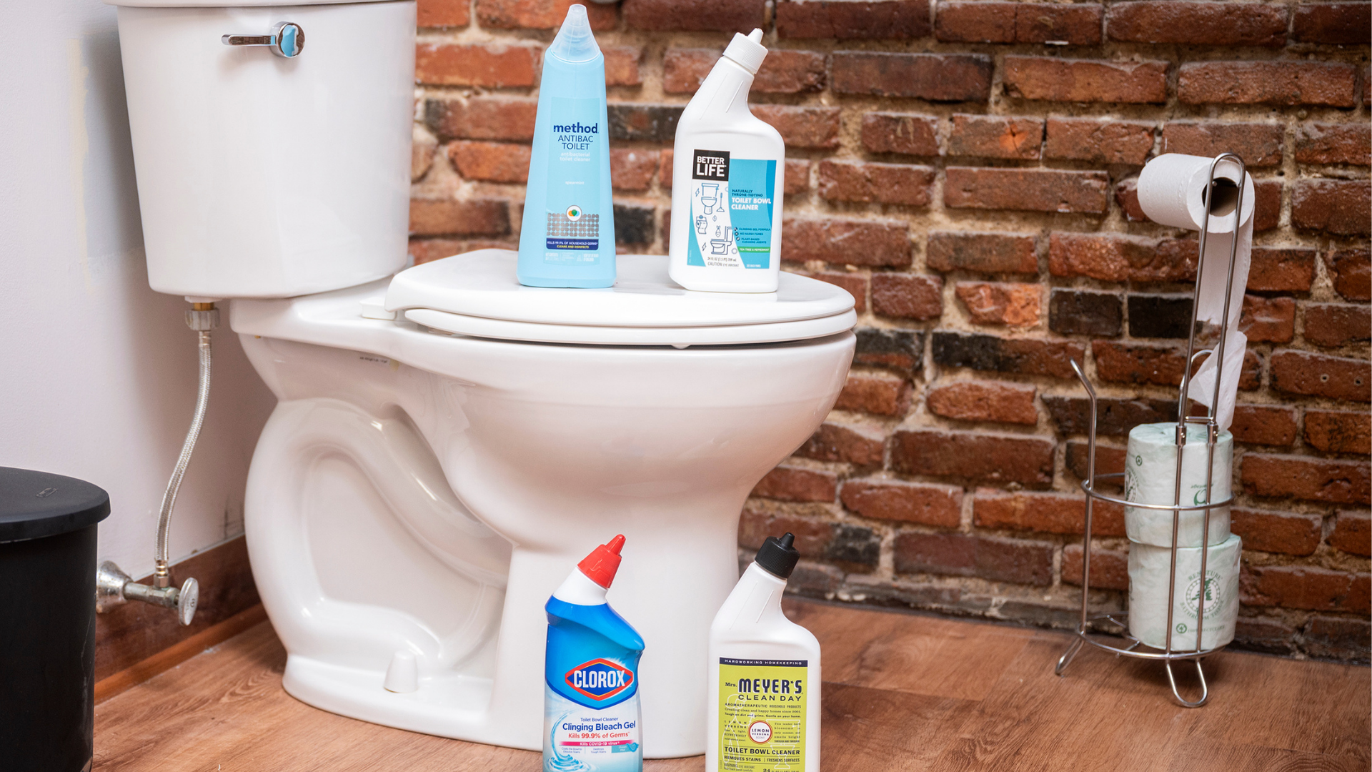 Four bottles of toilet bowl cleaner stand on top of and next to a toilet