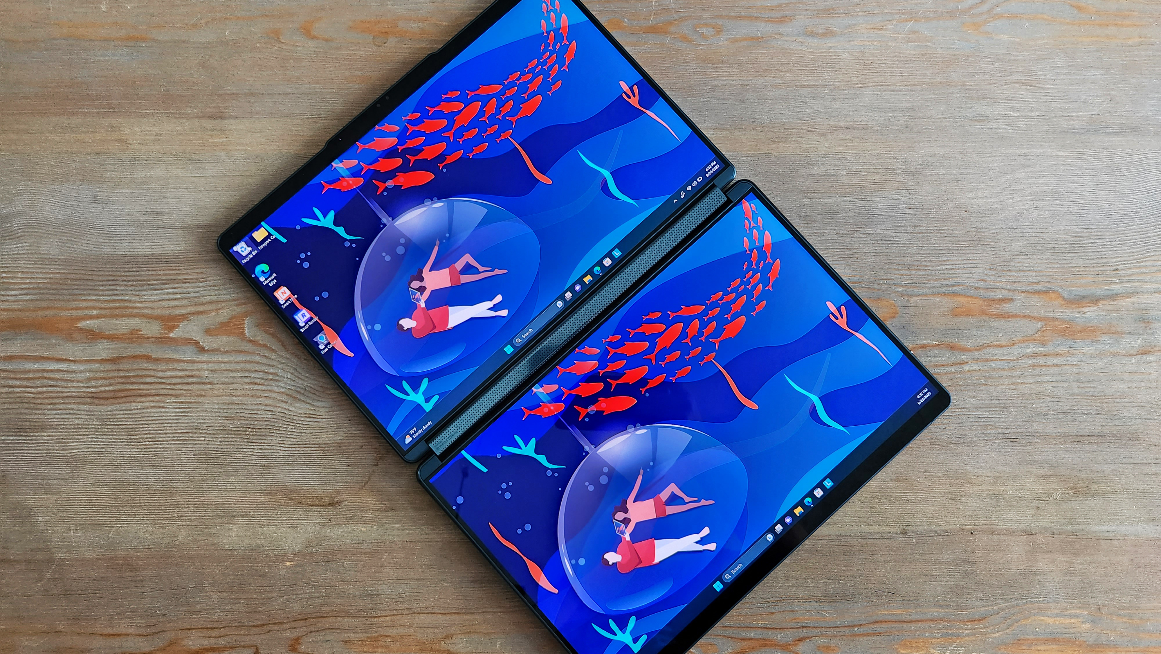Notebook s dvoma obrazovkou zobrazuje farebné pozadie ležiace plochými pri drevenom povrchu