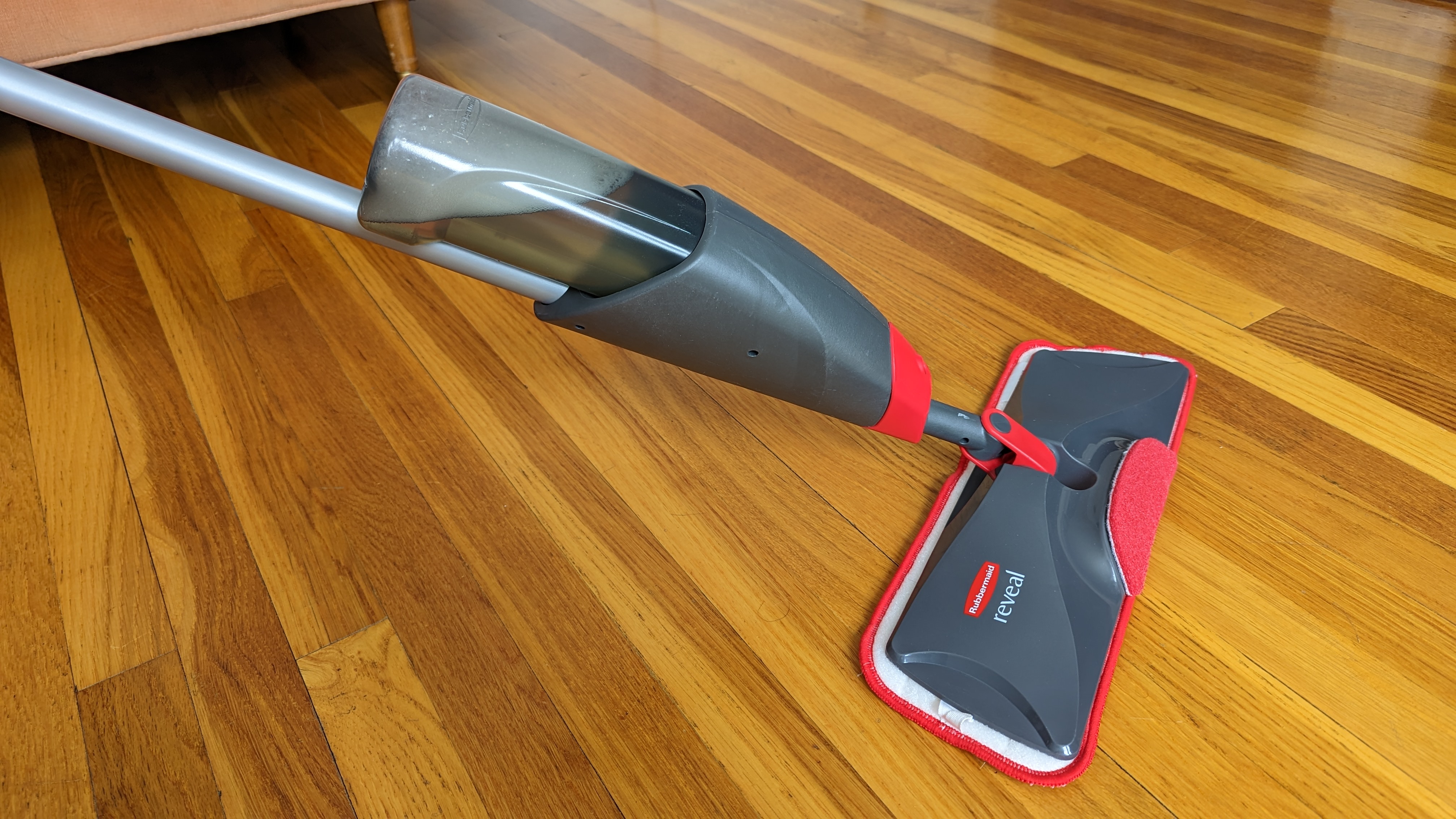 A gray and red mop with microfiber pad pushes across a hardwood floor