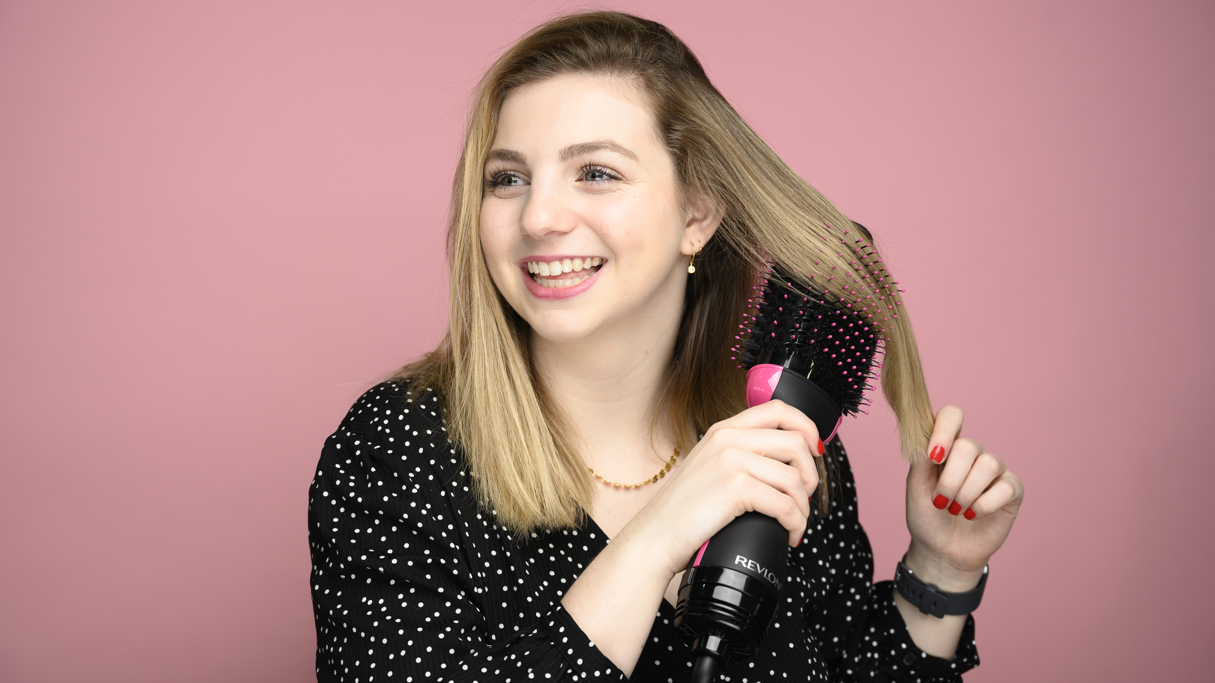 A woman brushing a hair dryer brush through her blond hair.