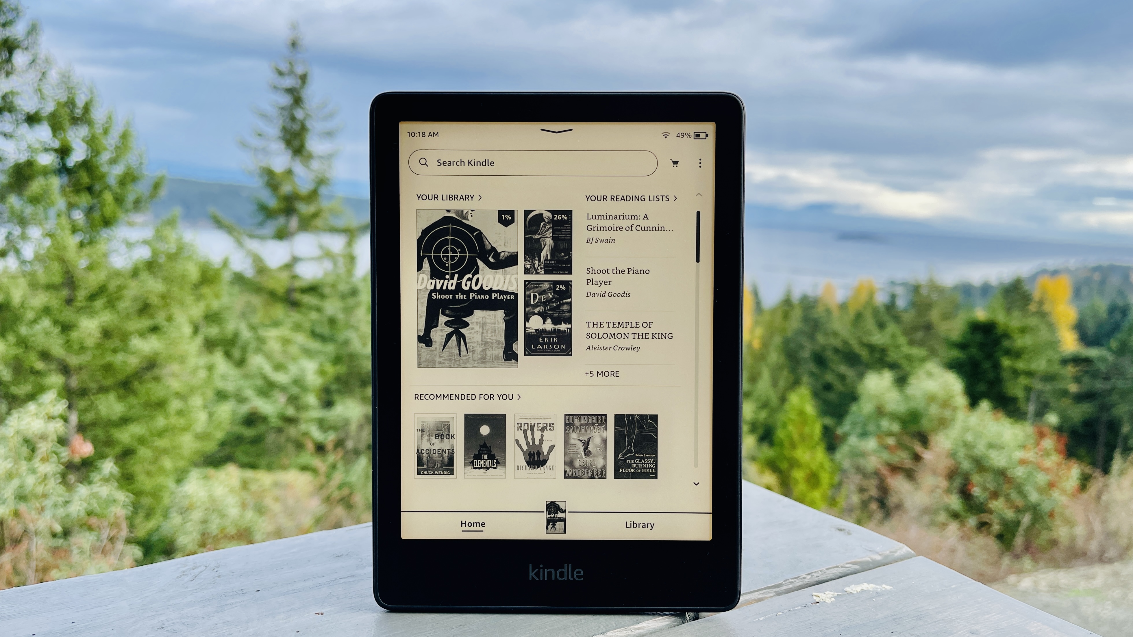 A Kindle Paperwhite sits on an outdoor table, against an overcast sky.