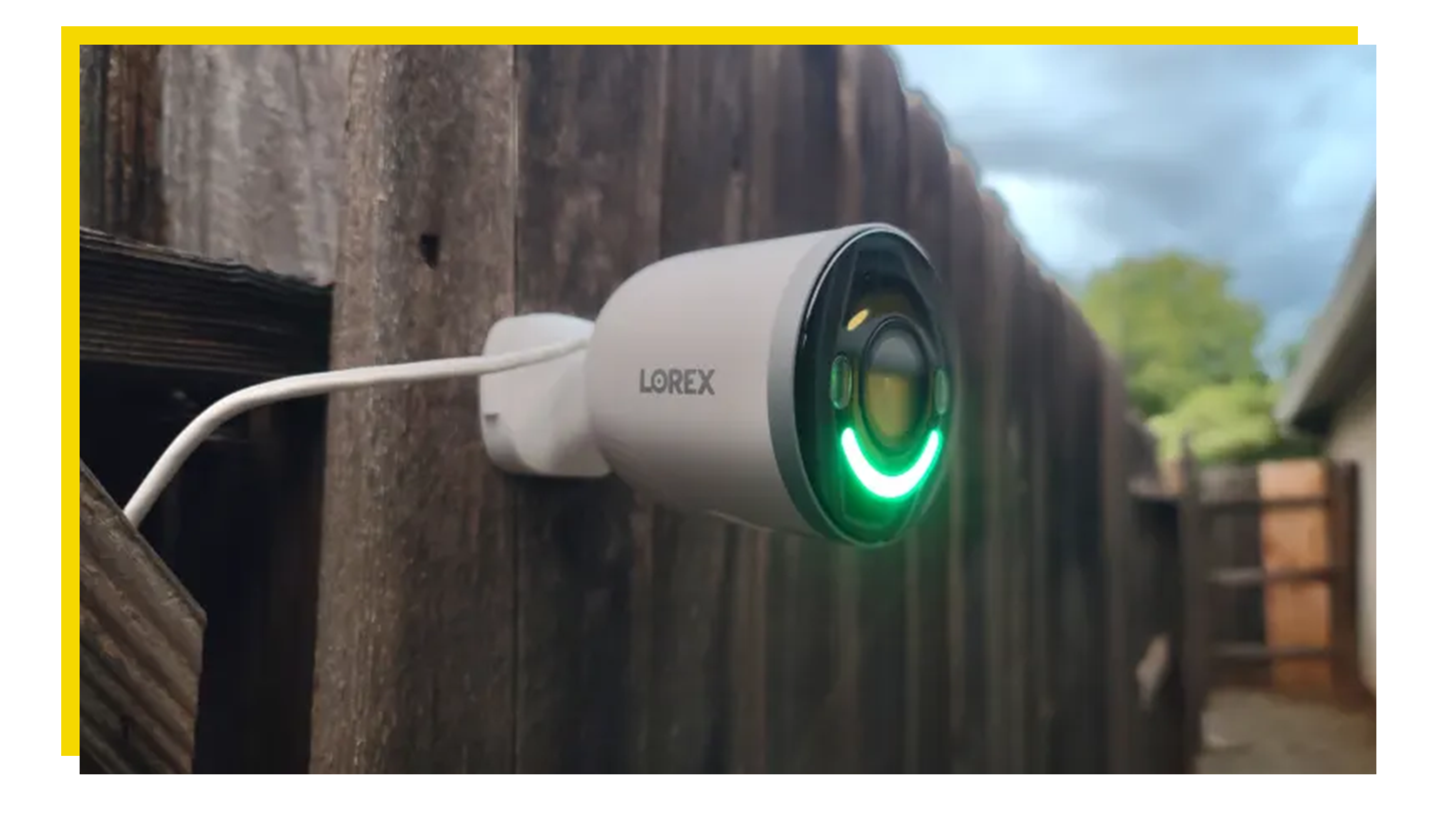 Lorex 4K 스포트라이트는 녹색 LED 조명으로 야외에서 나무 울타리에 장착되었습니다