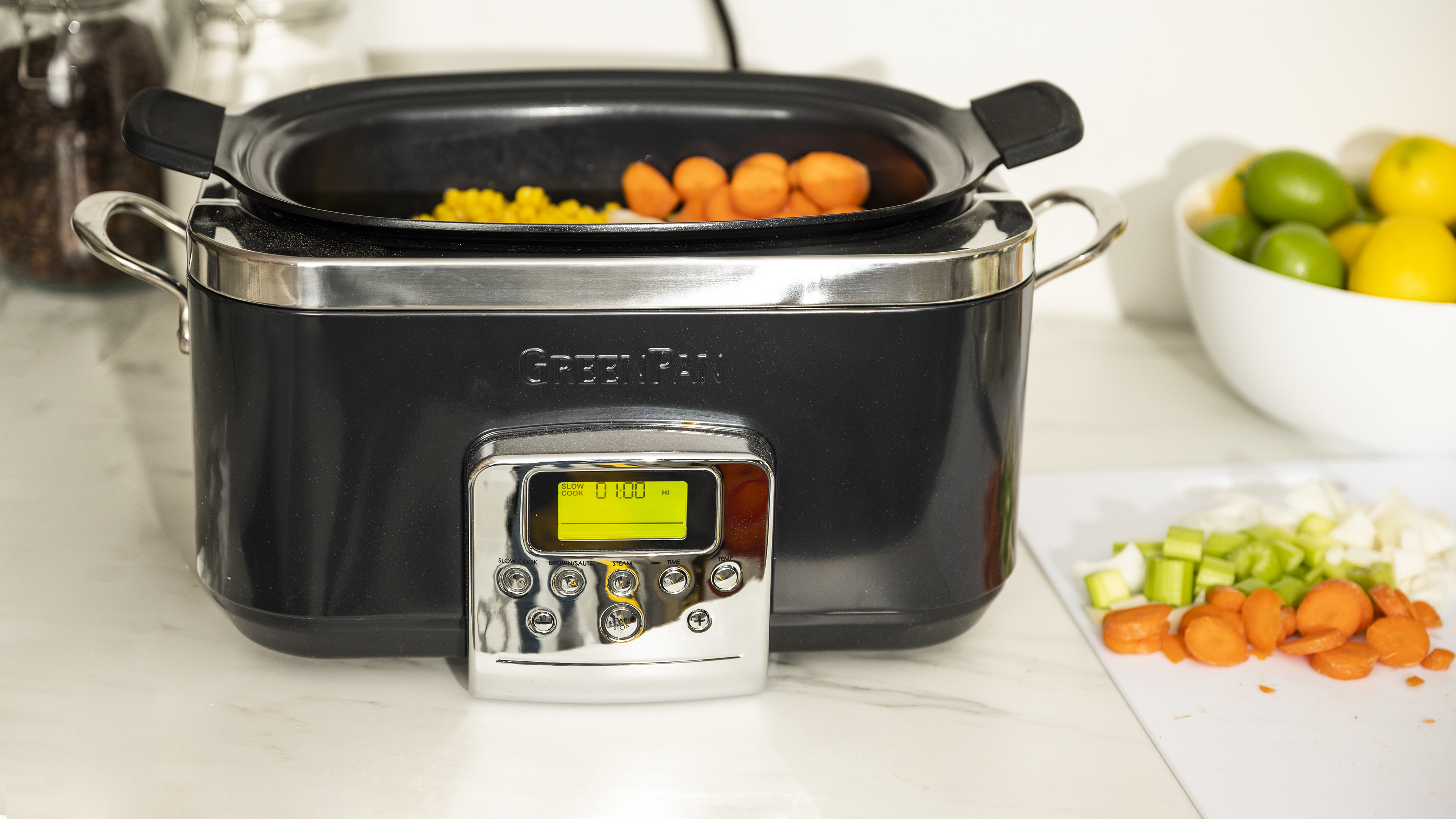 A black GreenPan Slow Cooker is filled with raw vegetables.
