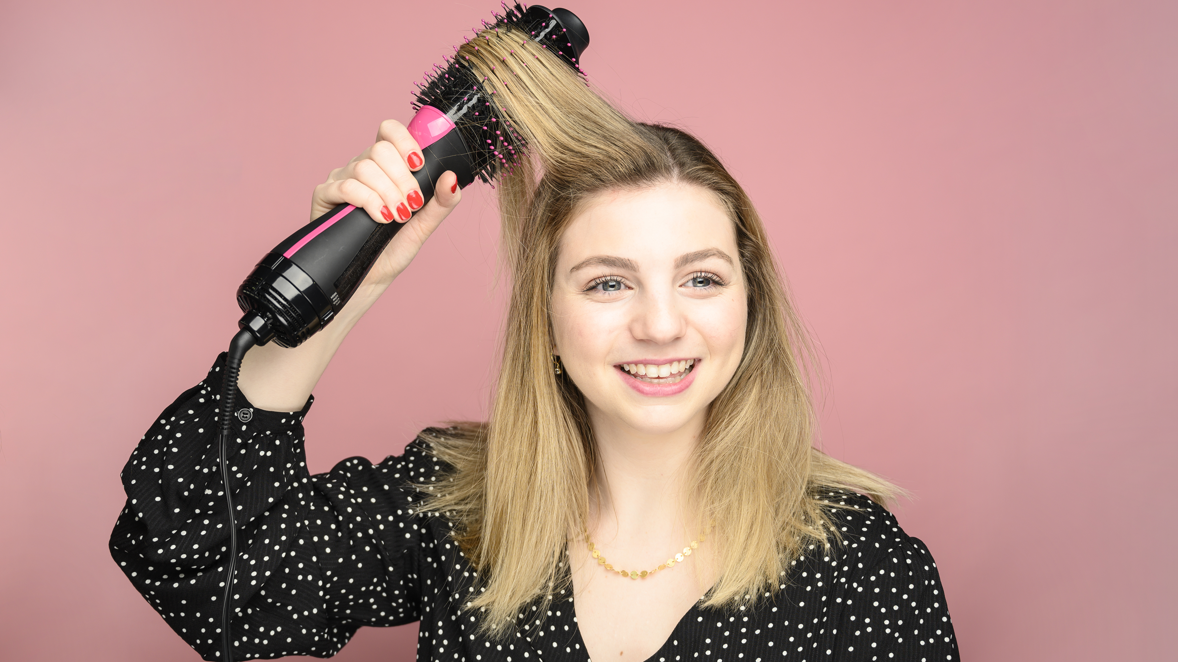 A woman running a hair dryer brush through her blond hair.